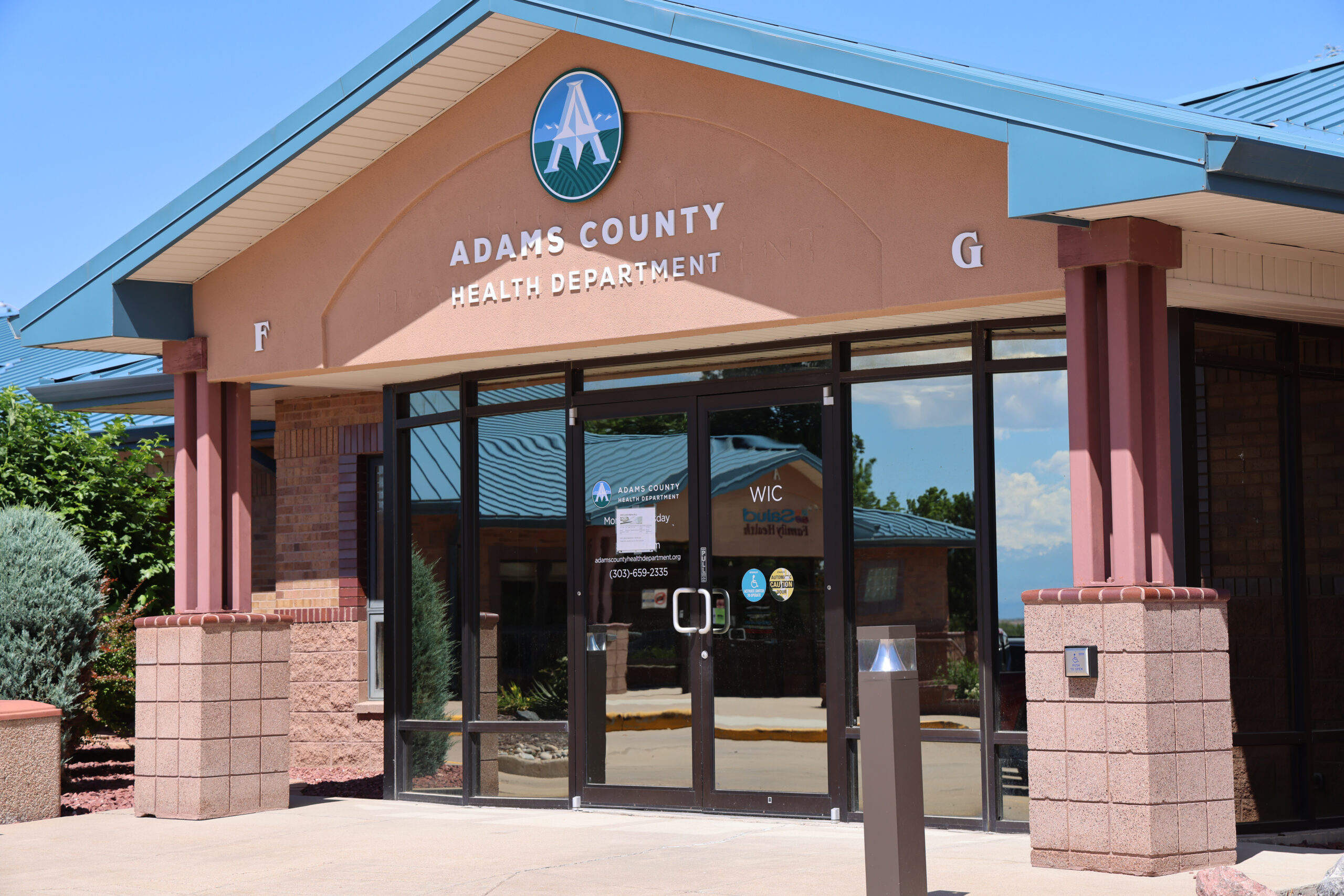 Adams County Health Department entrance with glass doors, logo above, and contact details on door.