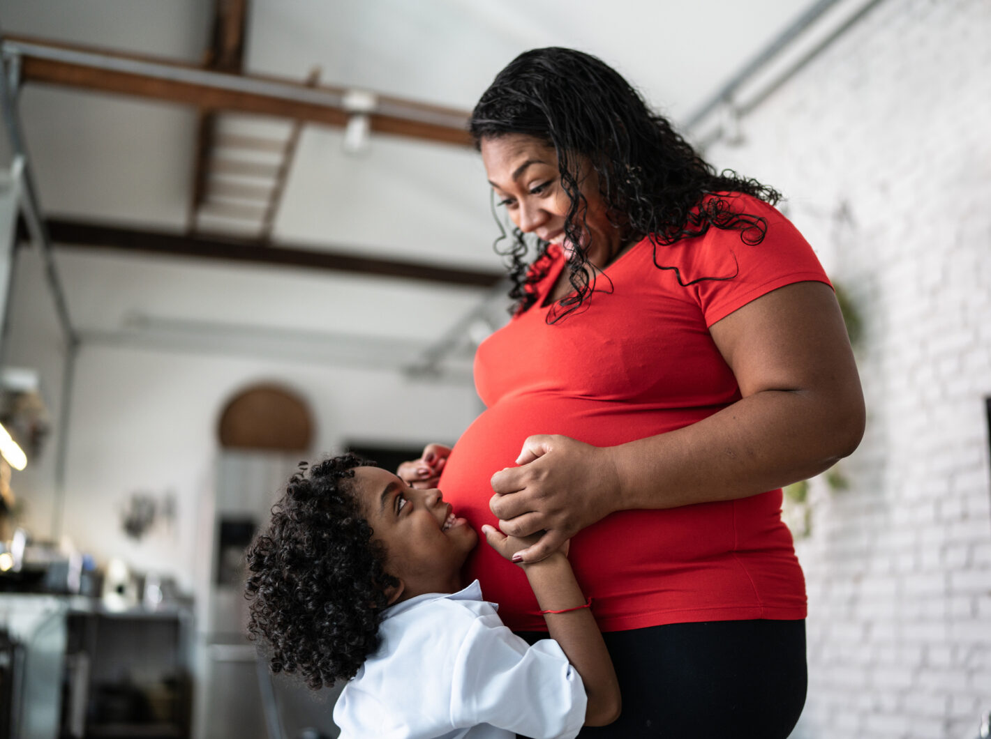 Smiling child hugs a pregnant woman's belly in a warm moment.