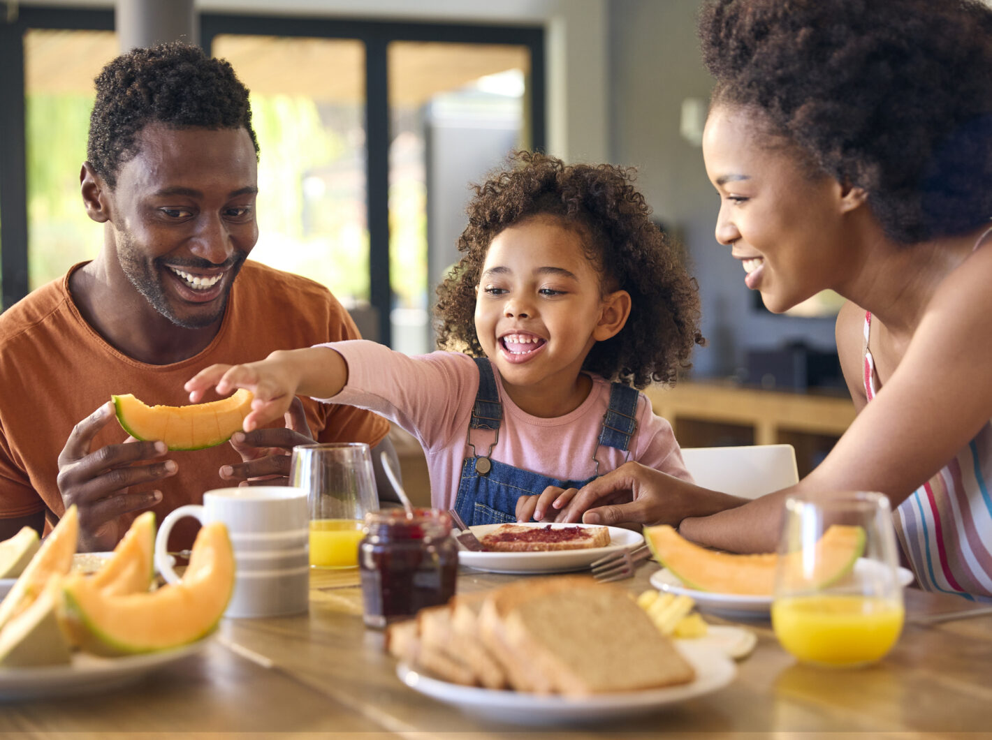 Family enjoying breakfast with melons, juice, and laughter