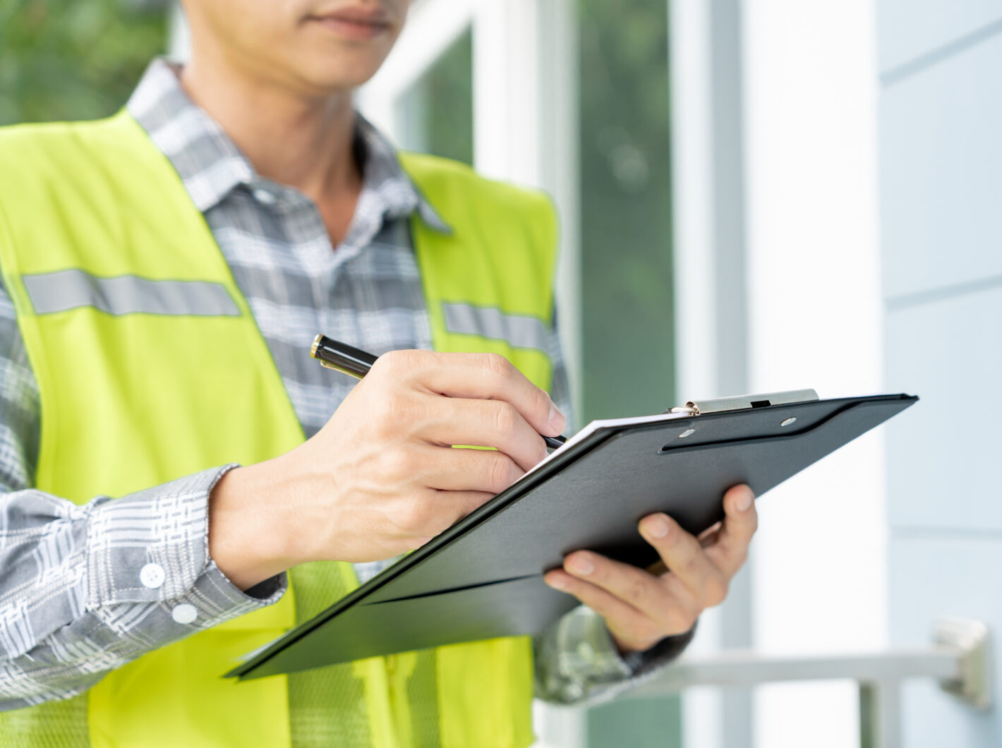 Person in reflective vest writing on clipboard outdoors