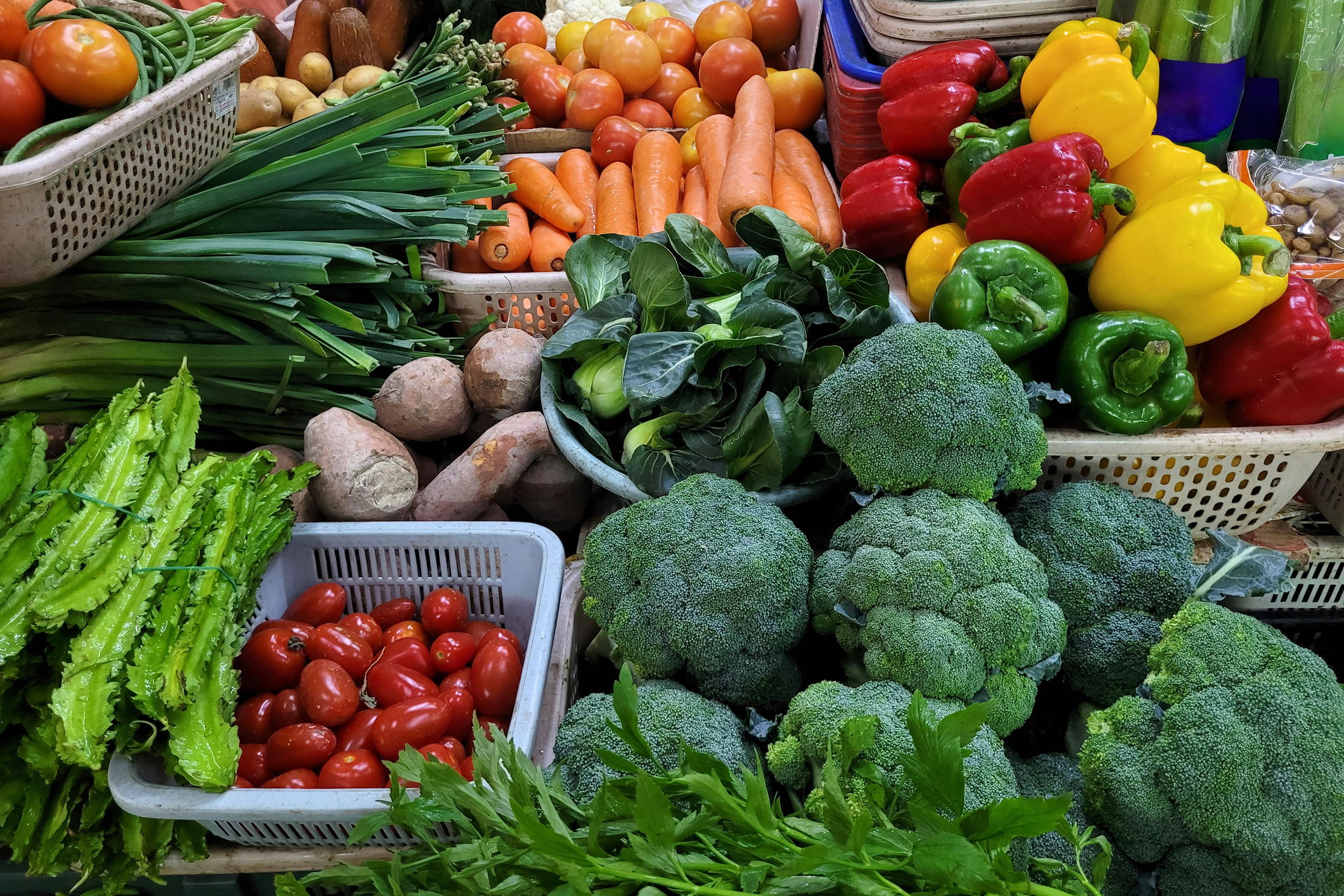 Assorted fresh vegetables including carrots, bell peppers, broccoli, and tomatoes displayed at market.