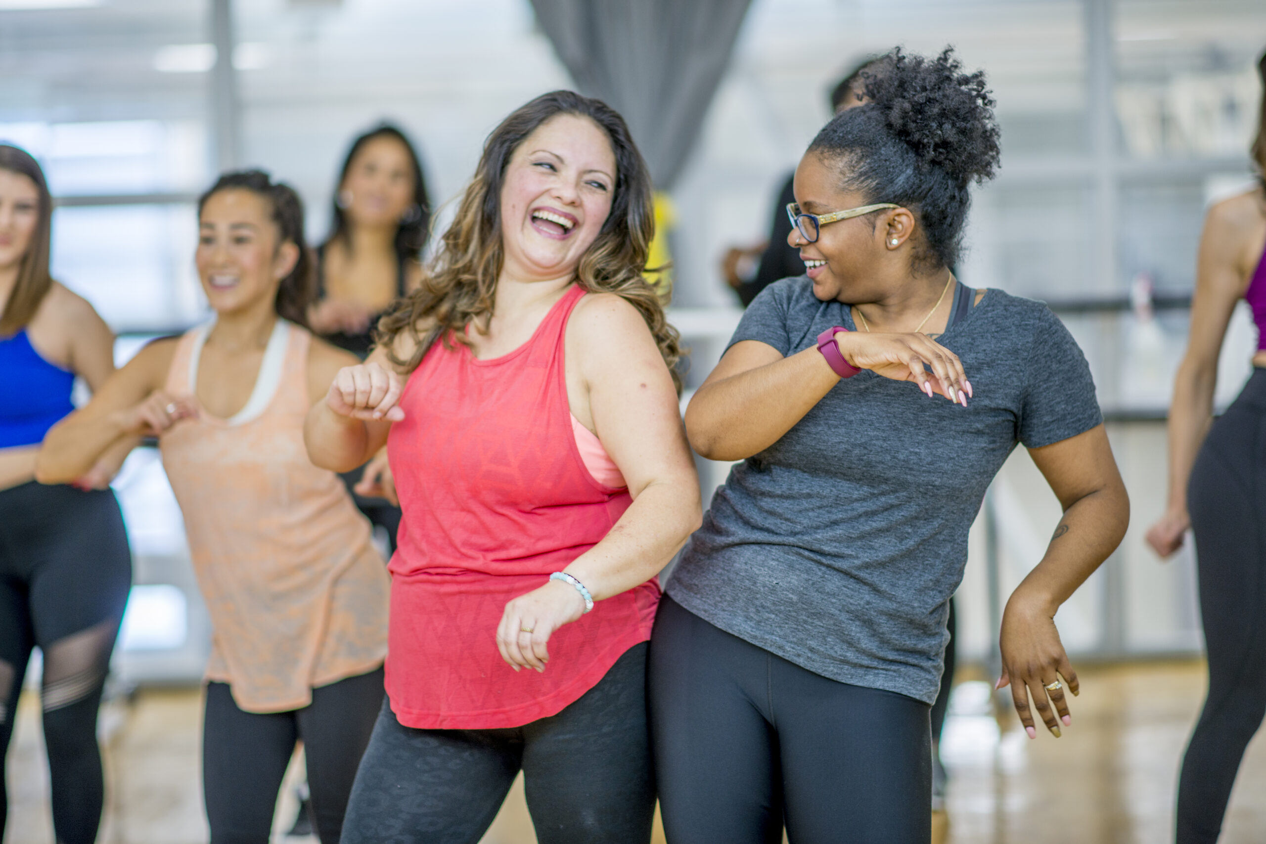 Women joyfully dancing in a fitness class, smiling and moving energetically.