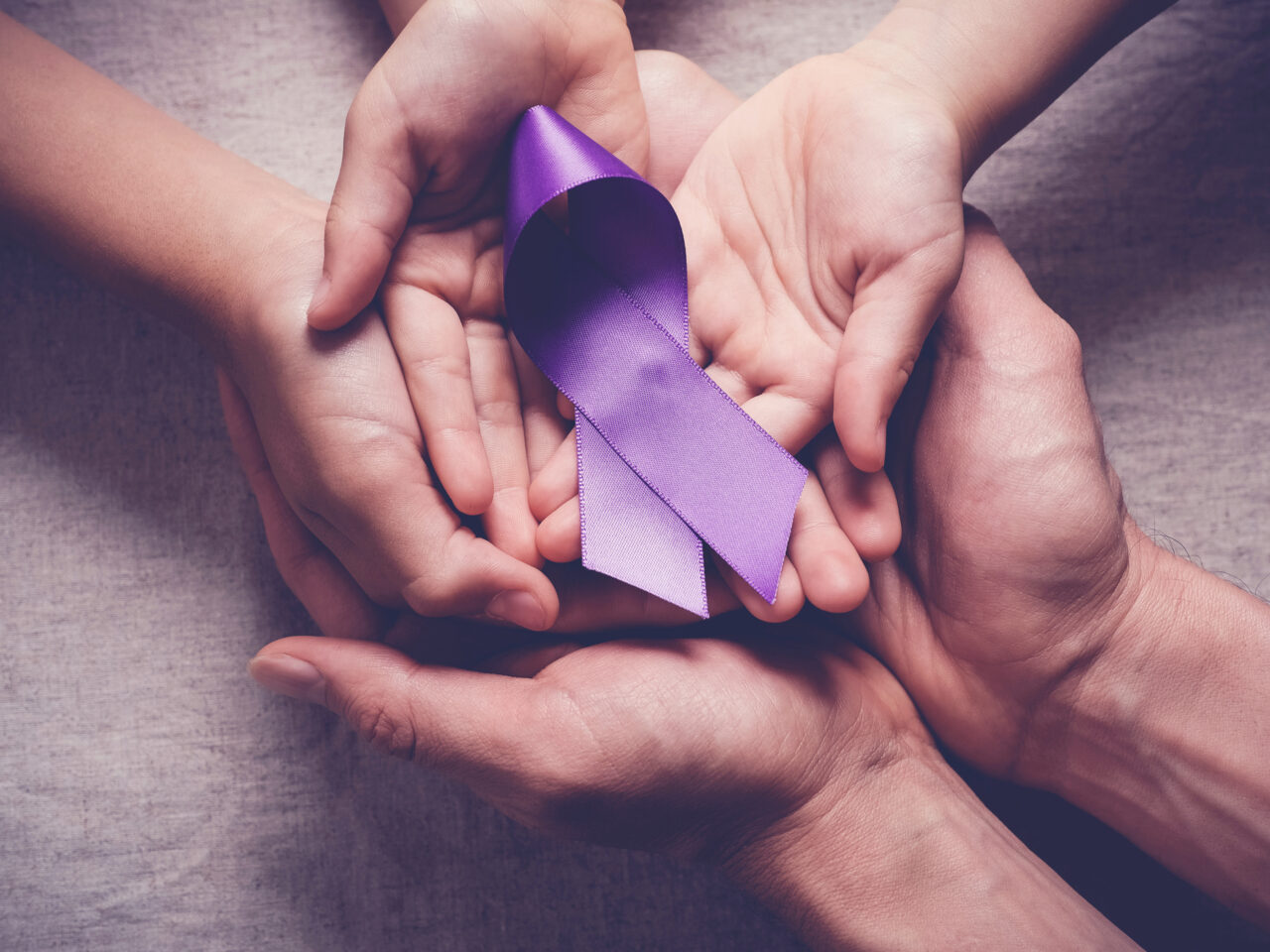 Hands holding a purple ribbon symbolizing support or awareness.