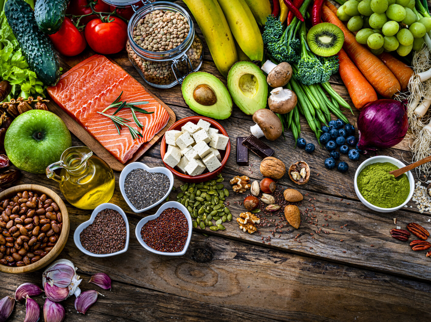 Photo of Aasorted healthy foods including salmon, avocados, nuts, fruit, and vegetables on a rustic wooden table