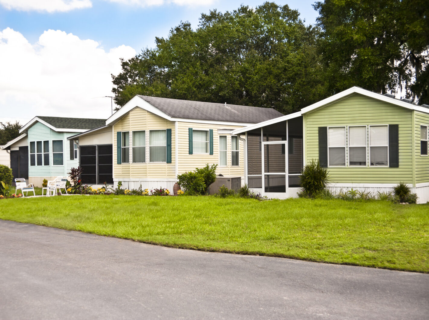 Photo of three colorful mobile homes with chairs on a grassy lawn
