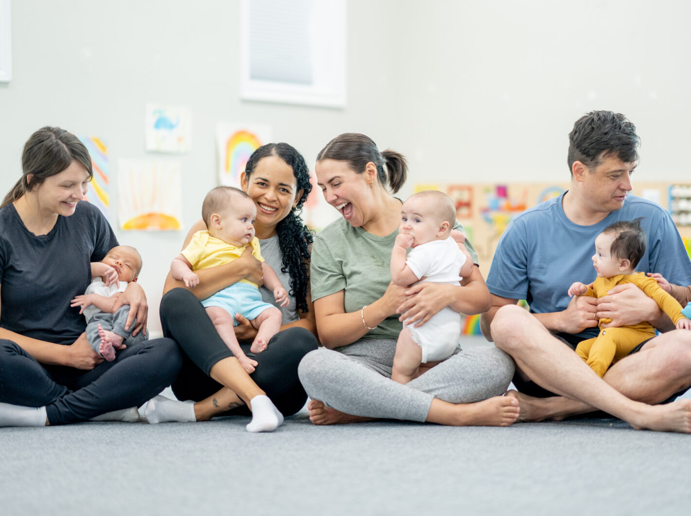 Photo of parents sitting on the floor with infants, engaging in a group activity.