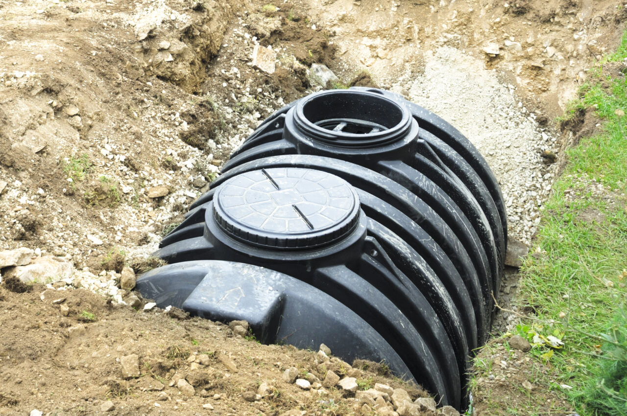 Photo of a black water tank partially buried in a trench, surrounded by gravel and soil.