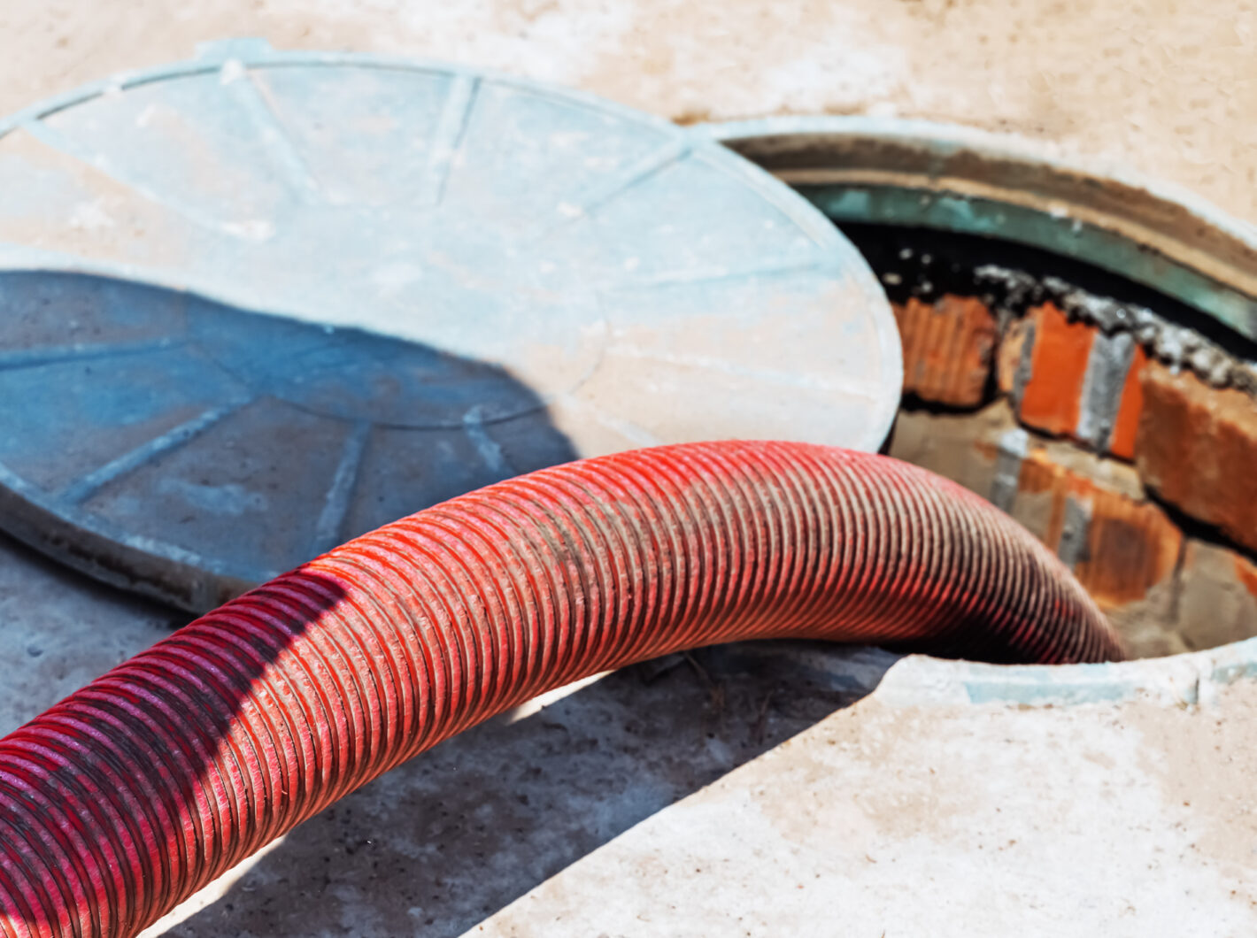 Photo of a red hose inserted into an open sewer manhole for maintenance