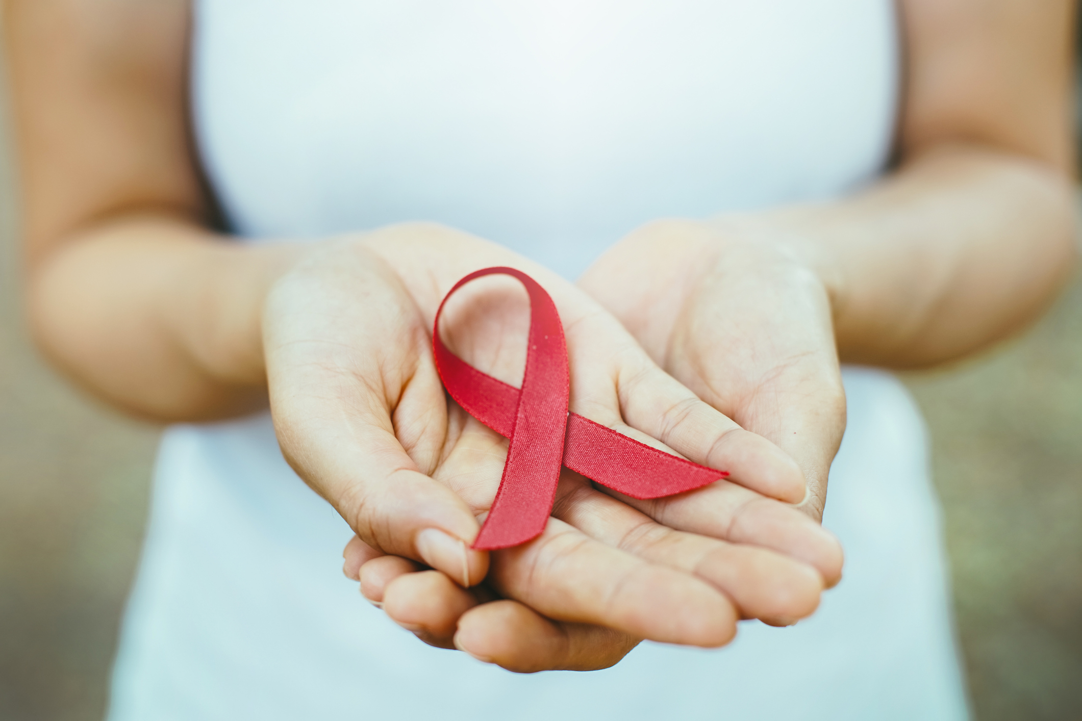 Photo of hands holding a red ribbon symbolizing HIV awareness